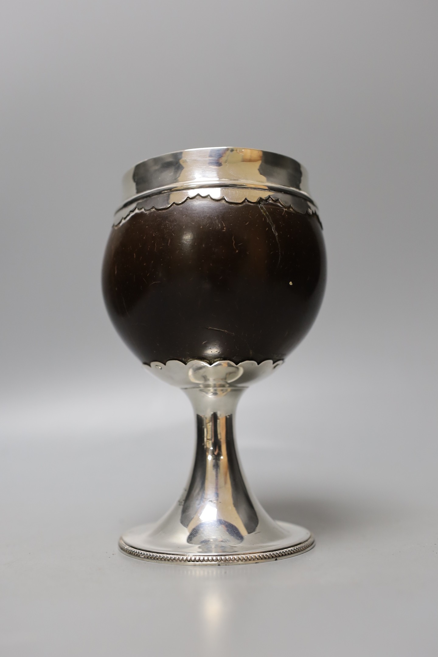 An early 19th century white metal mounted coconut cup, on pedestal stem, unmarked, height 15.6cm, gross weight 290 grams.